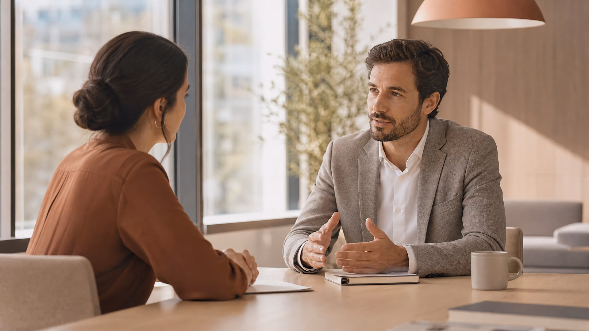 Man en vrouw in gesprek aan een tafel in een licht kantoor, de man gebaart terwijl hij praat